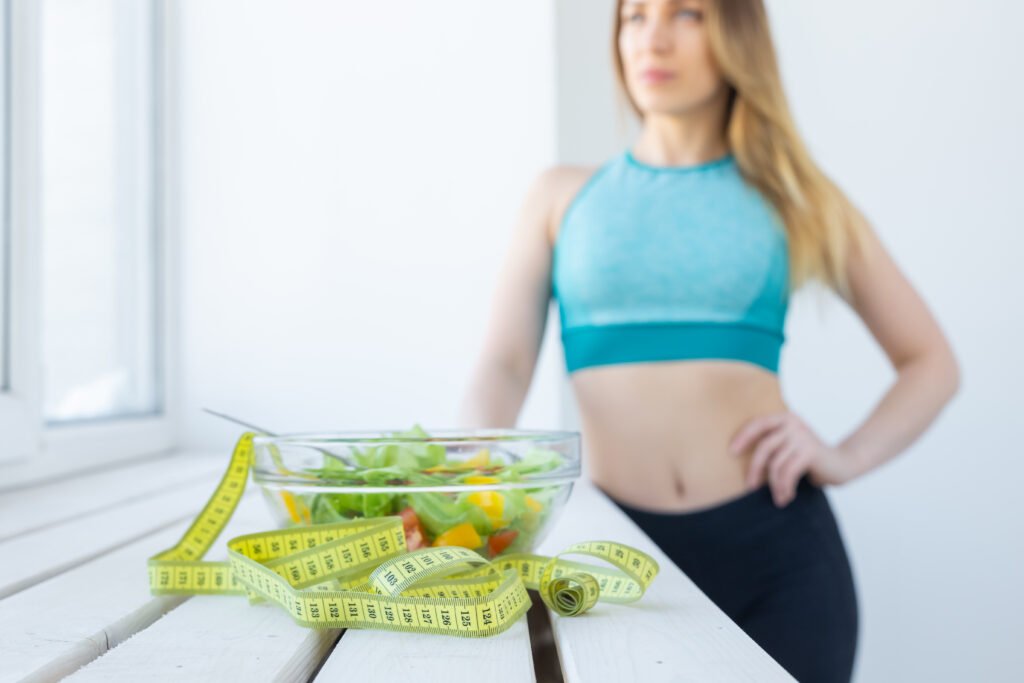 healthy lifestyle, fitness and diet concept close up dietary salad andmeasuring tape with woman in sports wear on background healthy lifestyle, fitness and diet concept close up dietary salad andmeasuring tape with woman in sports wear on background