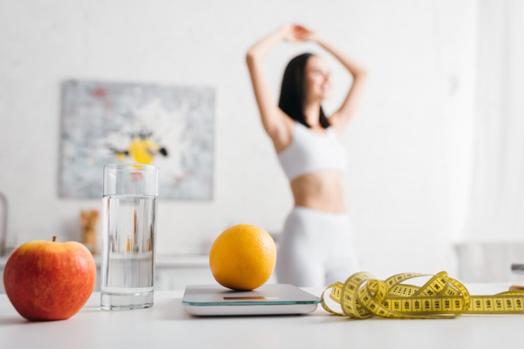selective focus of measuring tape, fruits with scales and glass of water on table and sportswoman in selective focus of measuring tape, fruits with scales and glass of water on table and sportswoman in